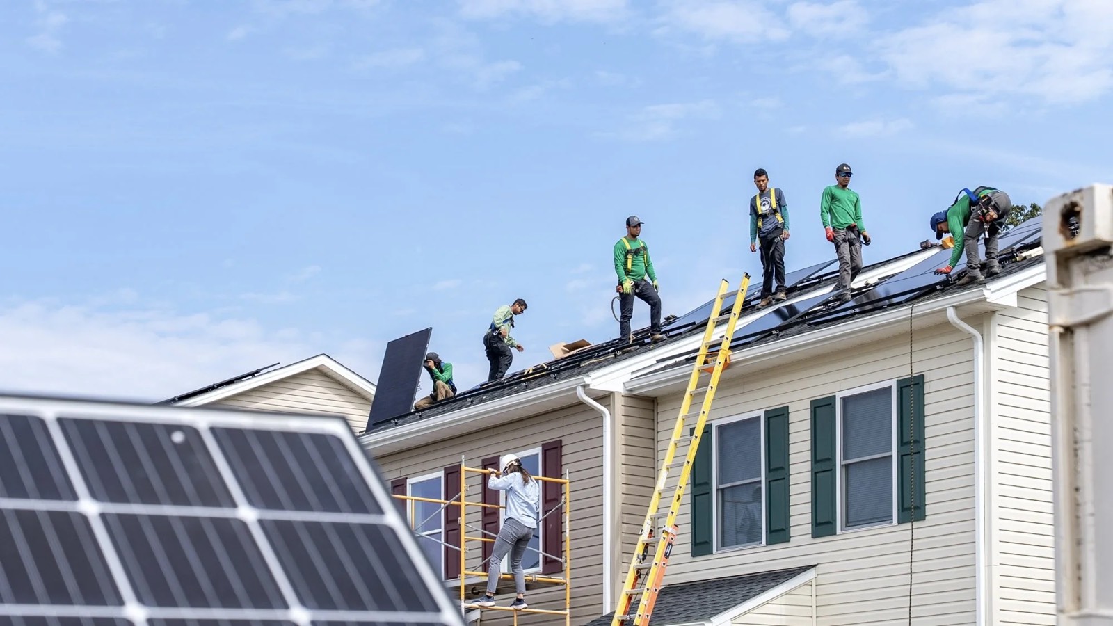 Volunteers on the roof of a Habitat home, laying solar panels across the shingles.