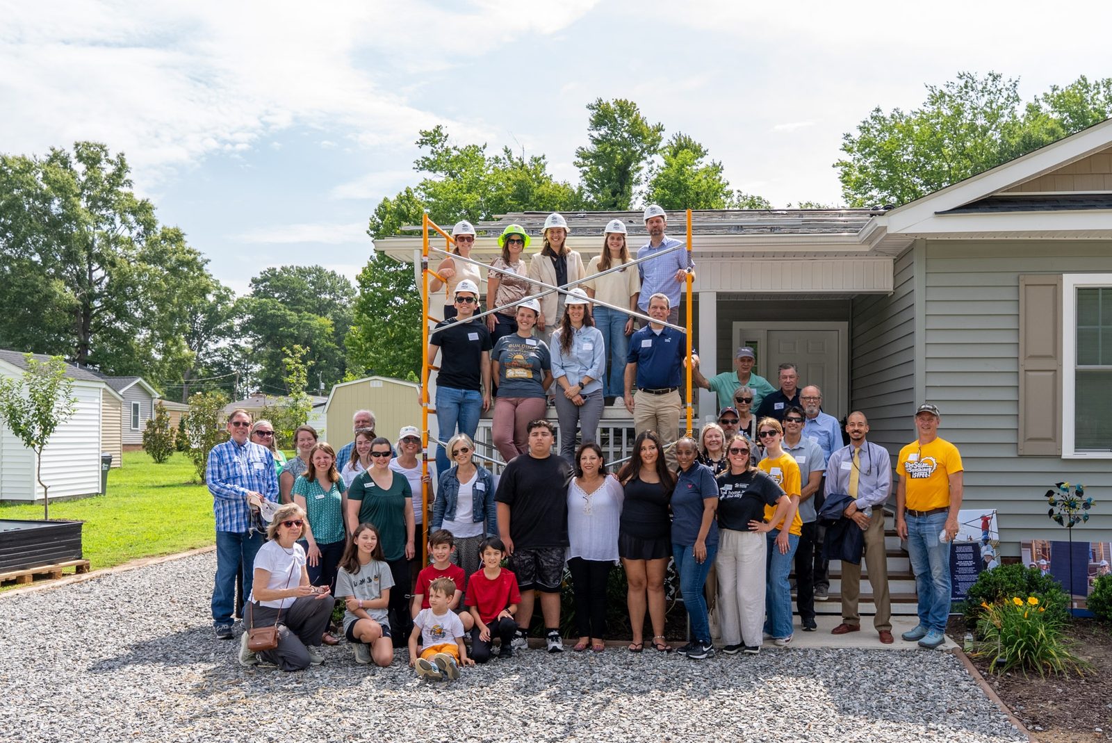 Volunteers, partners and Habitat families gathered on and around the porch of the hundredth Habitat home to get solar in Virginia, with panels staged on scaffolding beside them