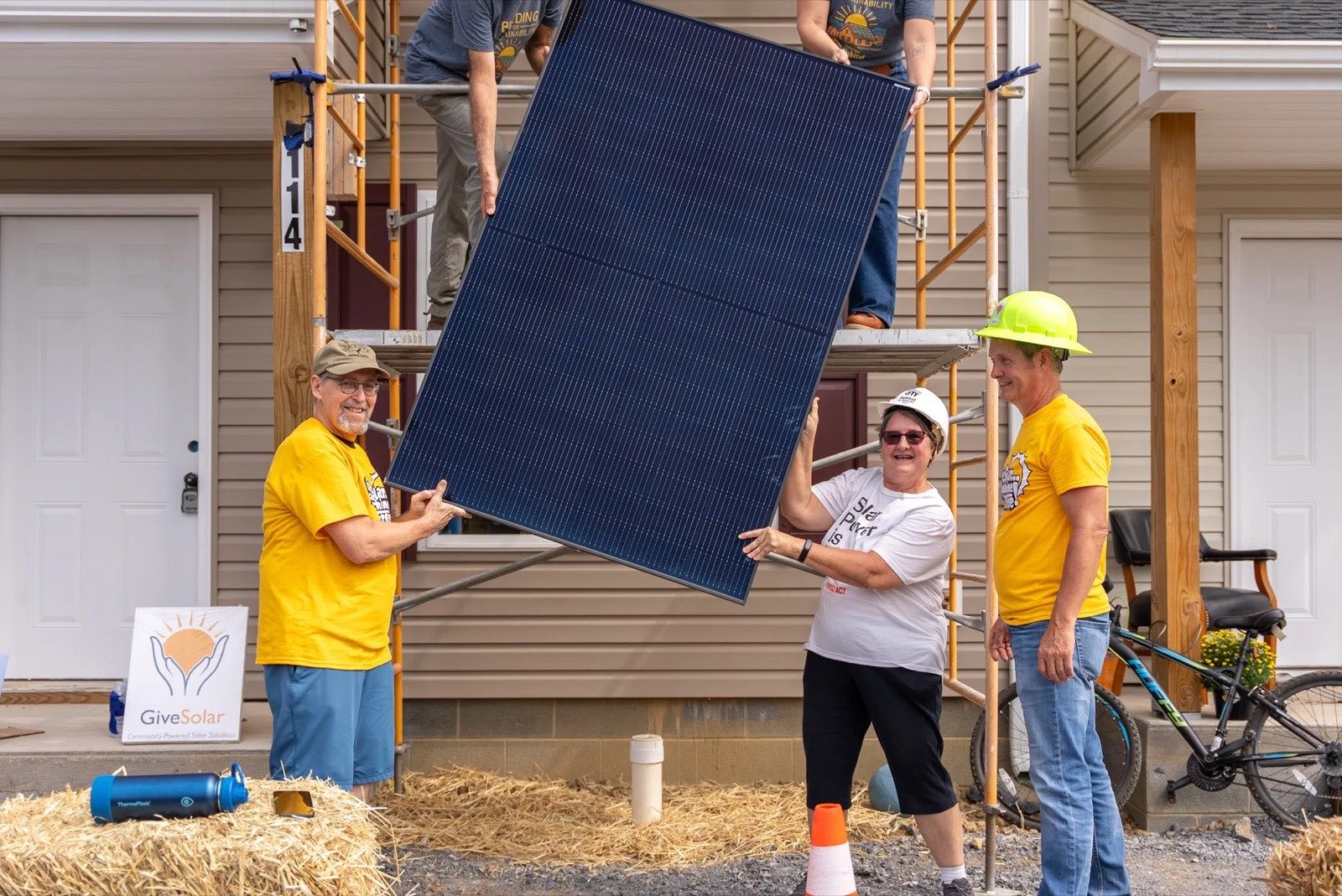Volunteers in hard hats passing a solar panel up toward the scaffolding at a Habitat build.